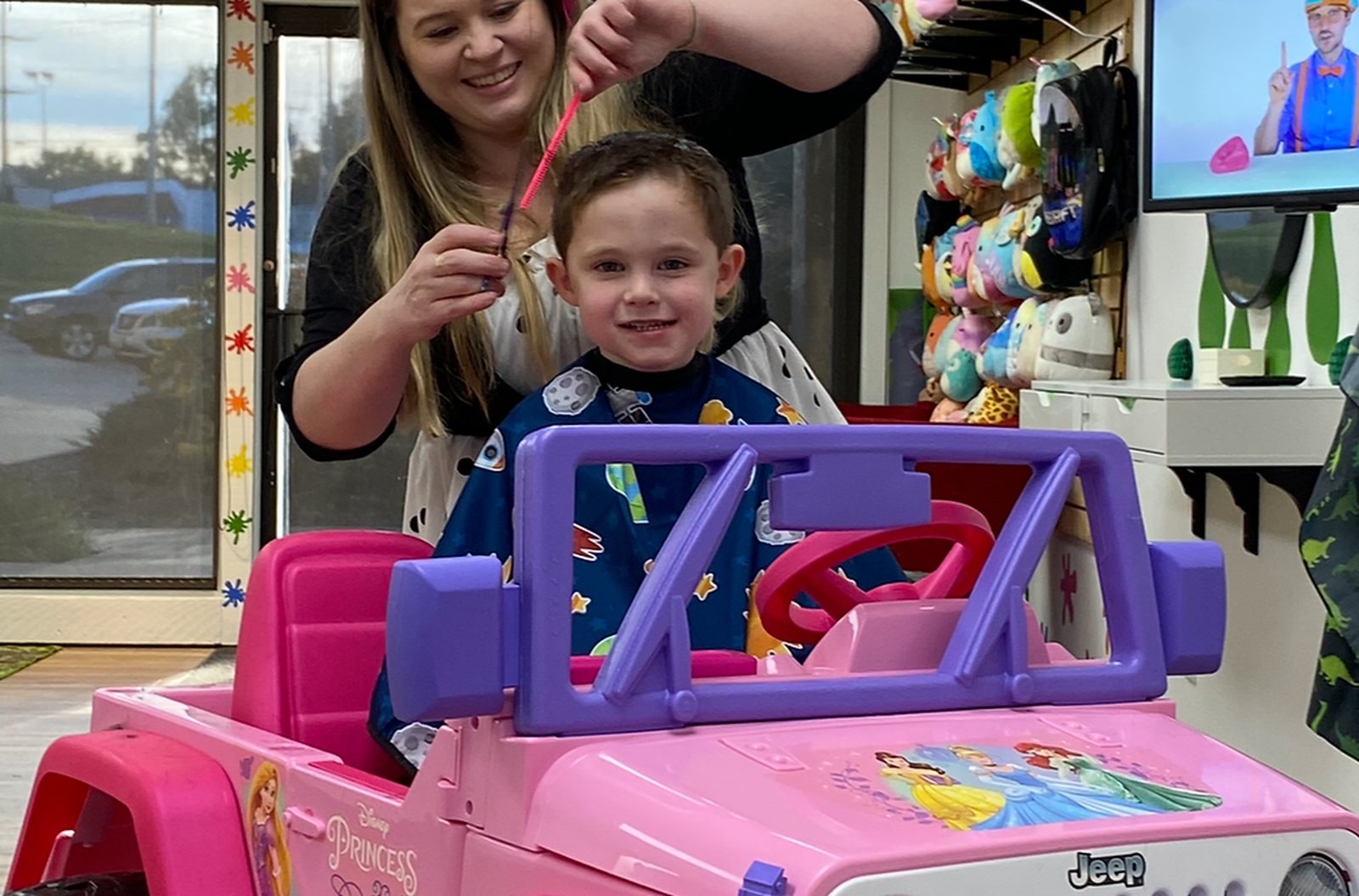 A child in a pink ride-on car in front of the storefront glass, which is covered in coloured paint splat decals.